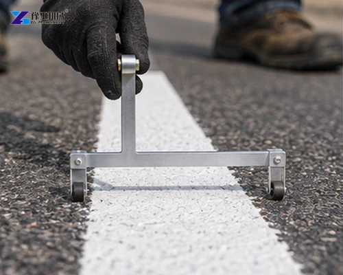 Handheld metal gauge checking the width of a white road stripe