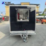 Towing end of a black catering trailer with an open hatch and guide wheel