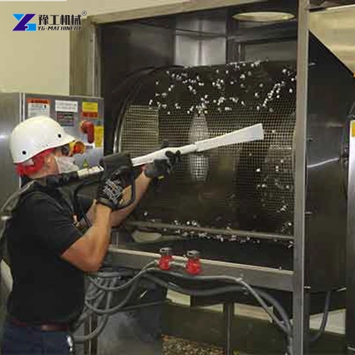 Operator aiming a dry ice blasting nozzle at industrial equipment